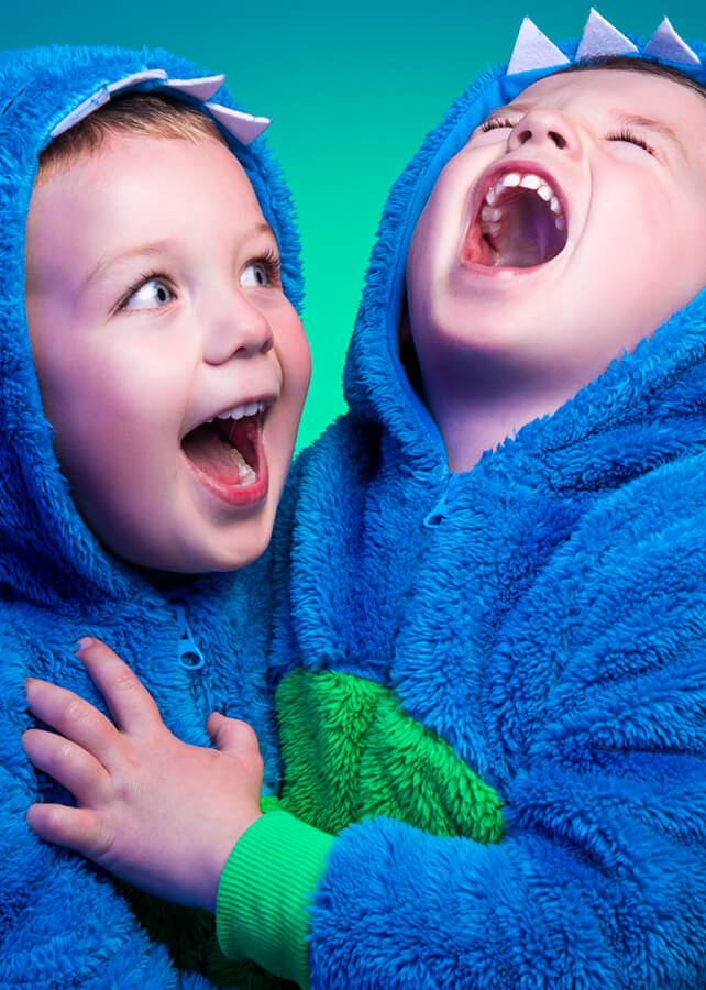 Child portrait of two brothers laughing and smiling in dinosaur onesies