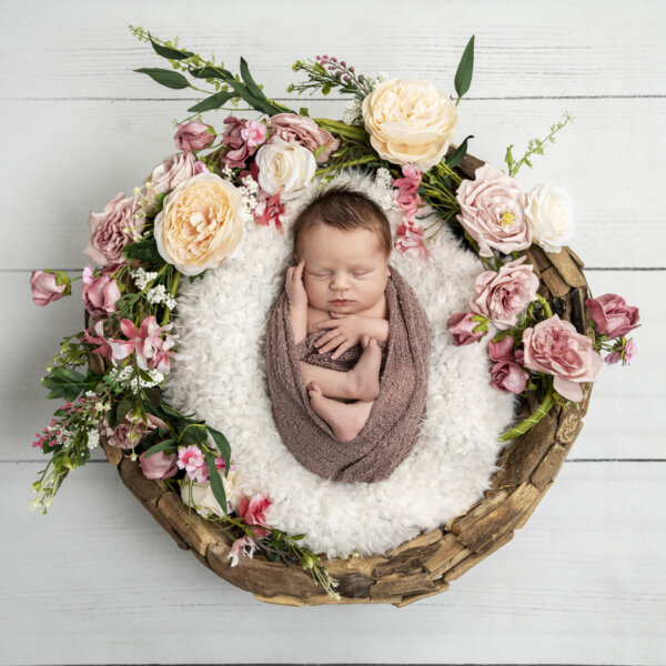 A baby wrapped up in a basket and surrounded by flowers