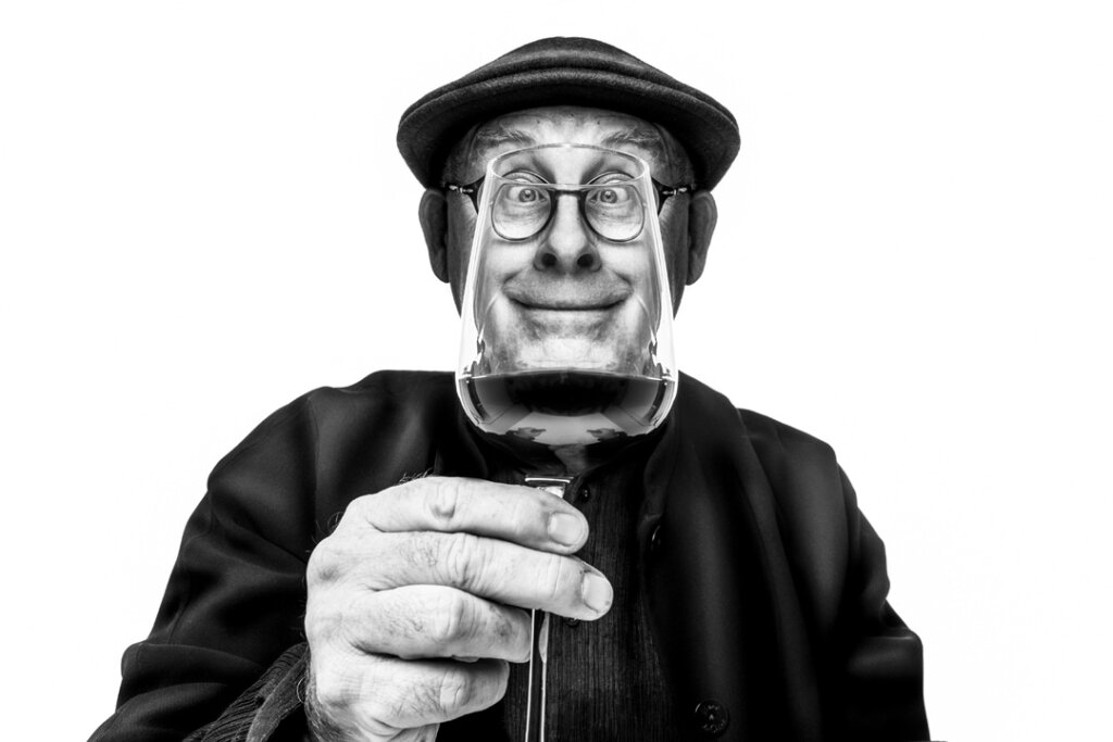 A black and white wide angle photograph of a man holding a wine glass